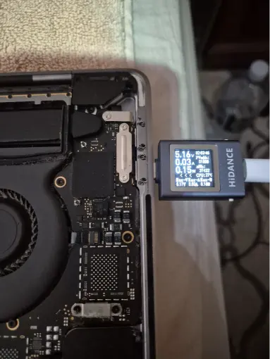 MacBook logic board being tested with USB-C power meter during diagnostic repair